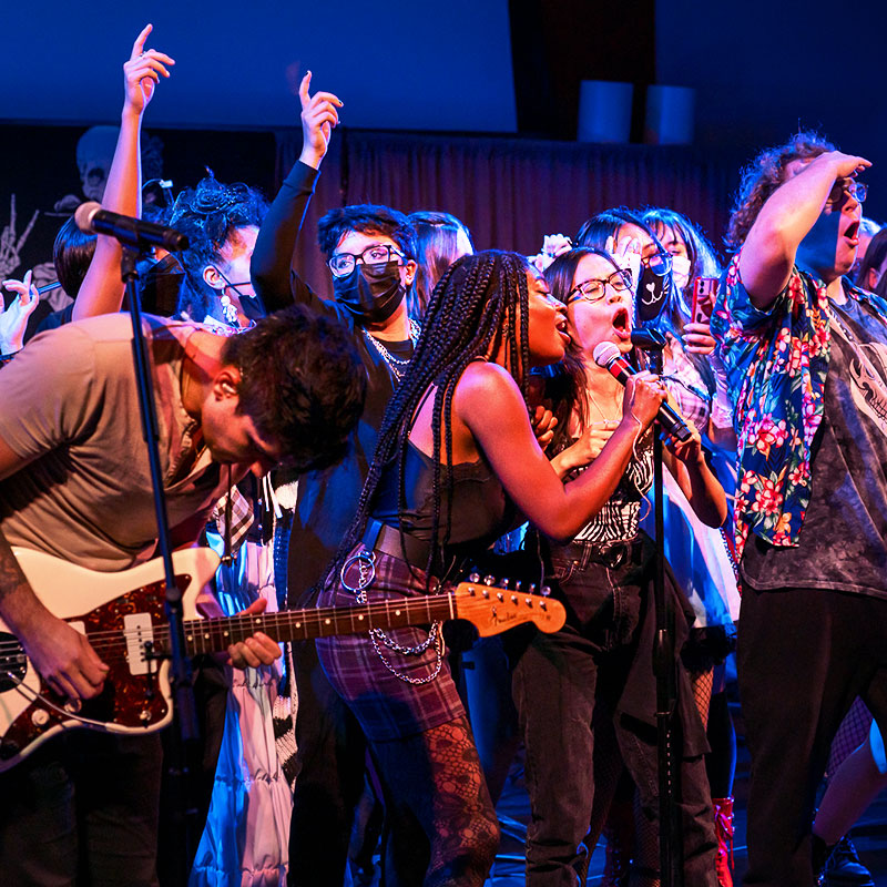 Group of students on stage singing and playing guitar